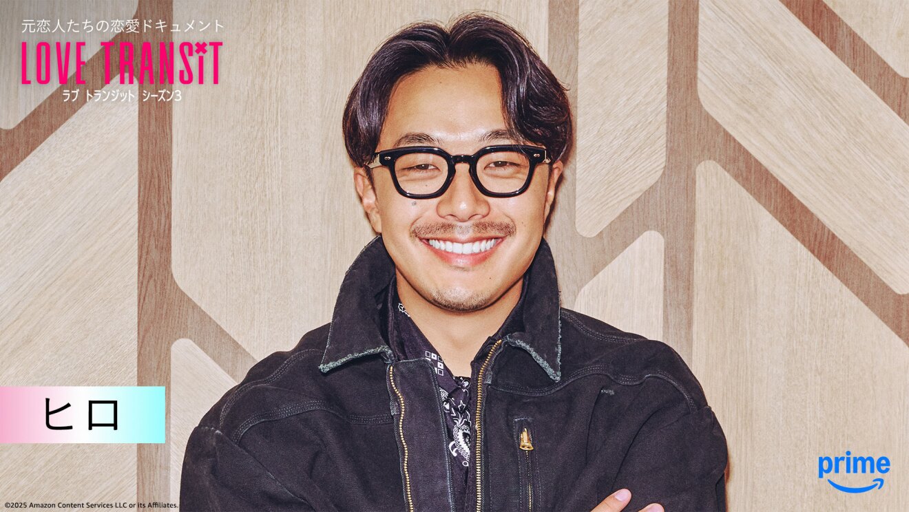 木目調の壁の前に立つ人物のバストアップ。デニムジャケット着用で、黒ぶち眼鏡。左上隅に「LOVE TRANSIT」の文字。左下に「ヒロ」と名前が表示されている。