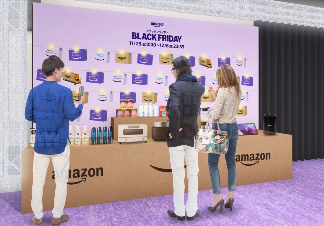 大きなAmazonダンボール箱と似ているテーブルの上には様々な商品が置かれている。そのディスプレイの前で男性2人と女性1人が商品を見ている