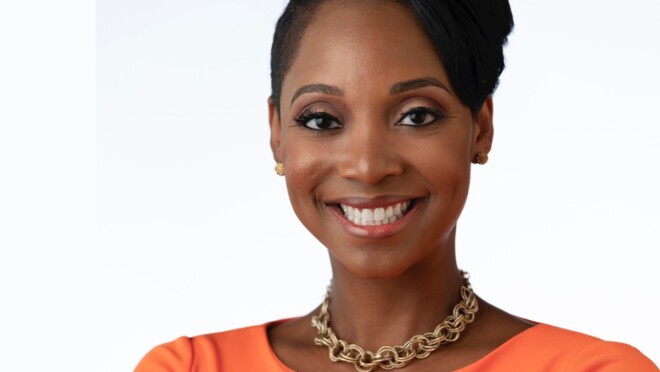 A woman smiles at the camera, her arms crossed in front of her.