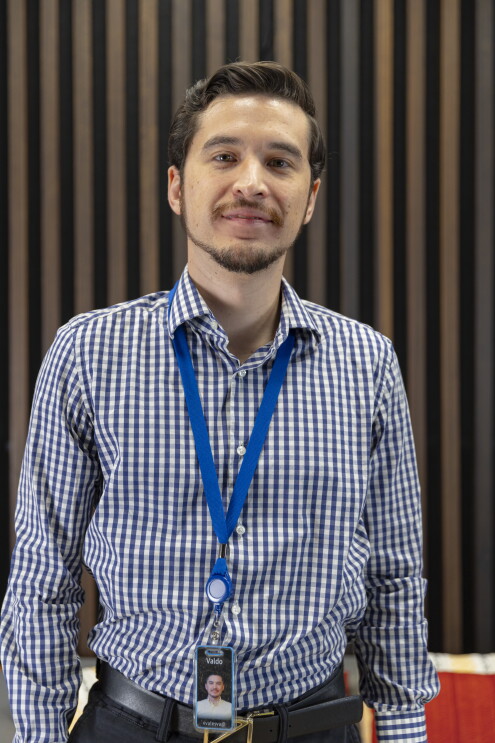 Foto de Valdo Vales, gerente de Finanzas en Amazon, de pie mirando a cámara con una camisa de cuadros. 