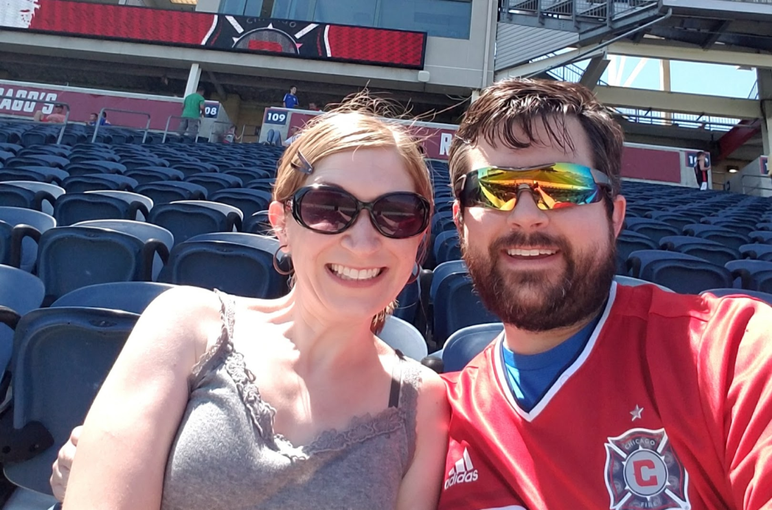 An image of a man and a woman smiling for a photo while sitting in the stands at a baseball game.