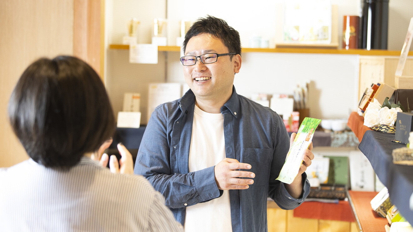 明るい店内でお客様に商品の説明をするメガネをした男性（岡さん）