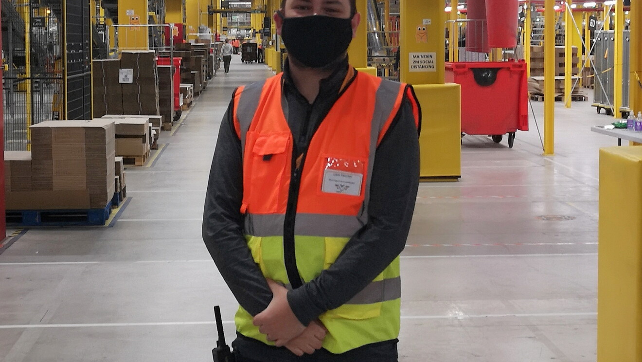 Liam Fletcher, WHS Coordinator at Amazon's fulfilment centre in Warrington, pictured wearing a high visibility vest and face mask.