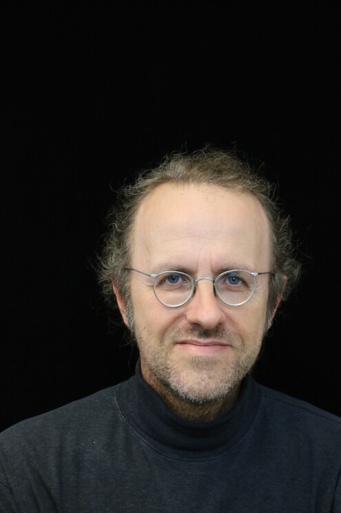 Bernhard Schölkopf, chief machine learning scientist for Amazon’s retail division, he wears a black turtle neck and wire framed silver glasses, and sits in front of a black background.