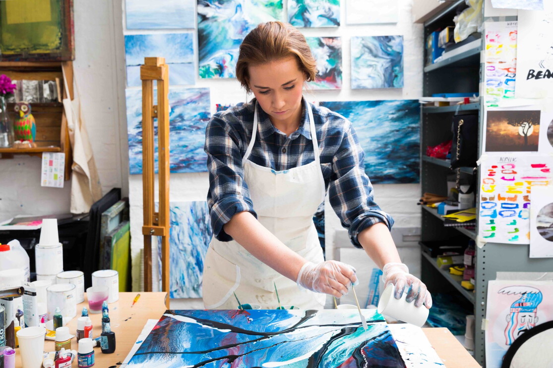 Kate Chesters creating a resin board using blue, red, purple and white resins. She working from her Liverppool based studio and there are lots of her artworks surrounding her. 