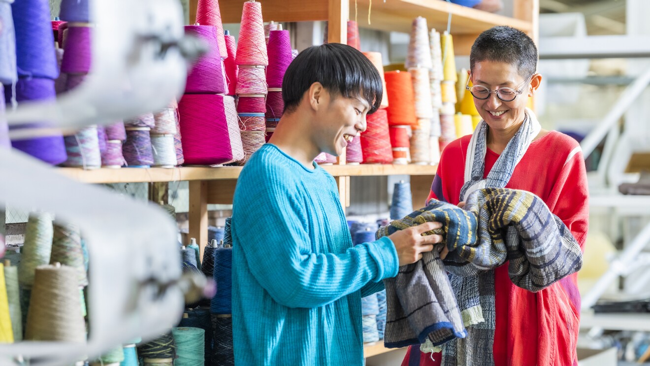 製品に触れながら、糸巻の棚の前でスタッフと会話する玉木さん
