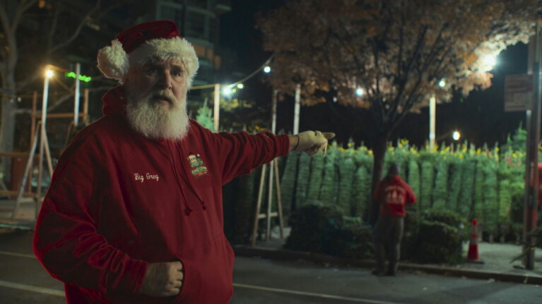 Big Greg from Merchants of Joy standing and pointing towards Christmas Trees