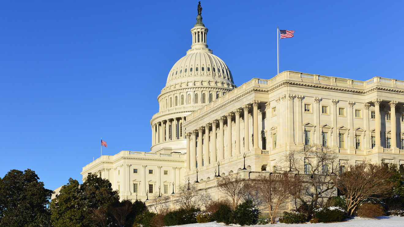 The U.S. Capitol building, on front of a blue sky. In the foreground, snow is on the ground. 