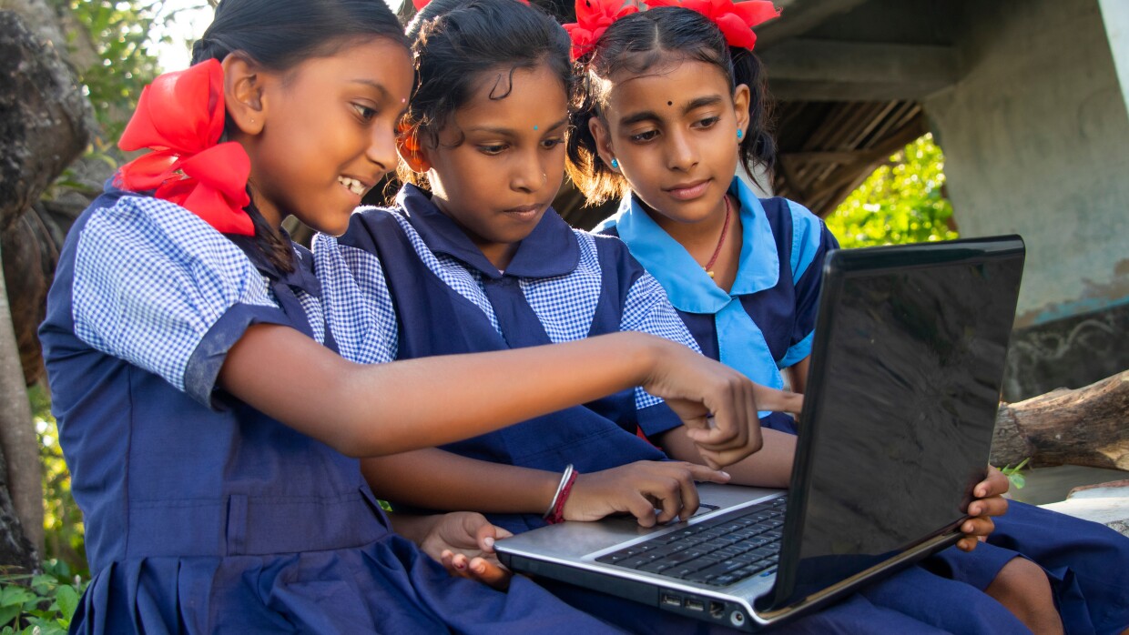 3 School girls sit together watching a laptopm