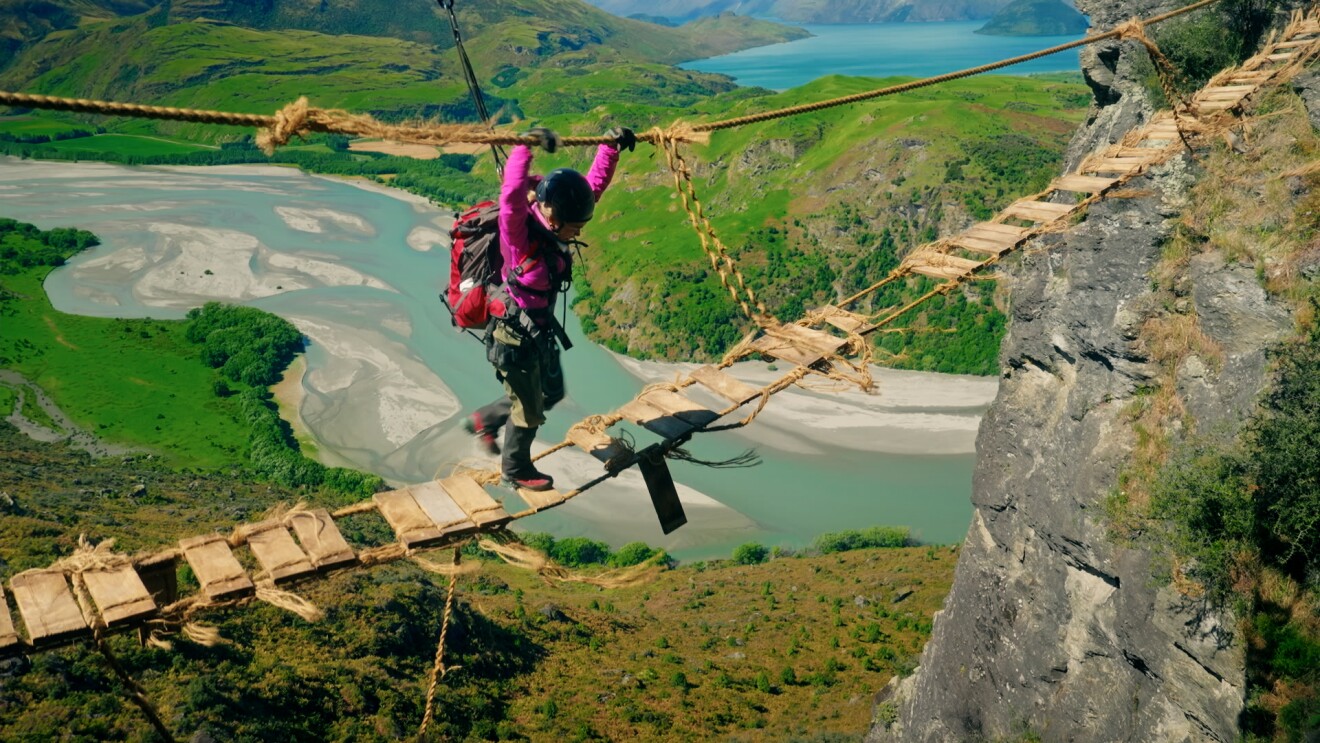 Wanderer überquert wackelige Seilbrücke über malerischem Flusstal