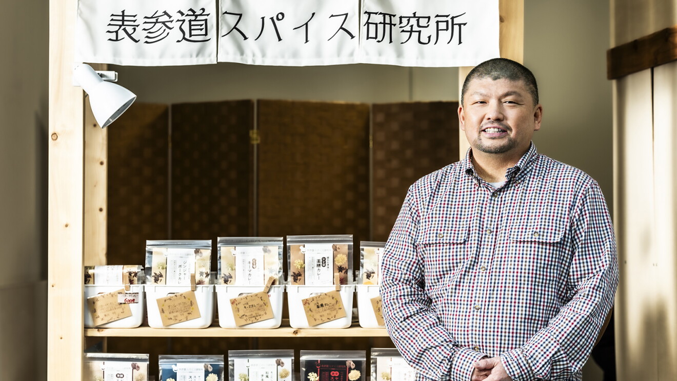「表参道スパイス研究所」と書かれたのれんが下がった店舗。並んだ商品を背にして立つ男性