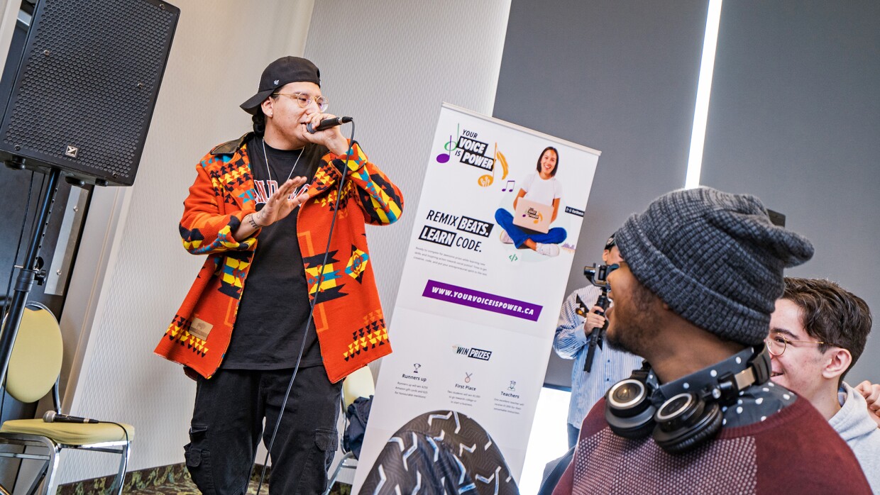 A photo of a performer holding a microphone and singing at Your Voice is Power, a school curriculum program and music remix competition that teaches coding skills using music from Indigenous artists.