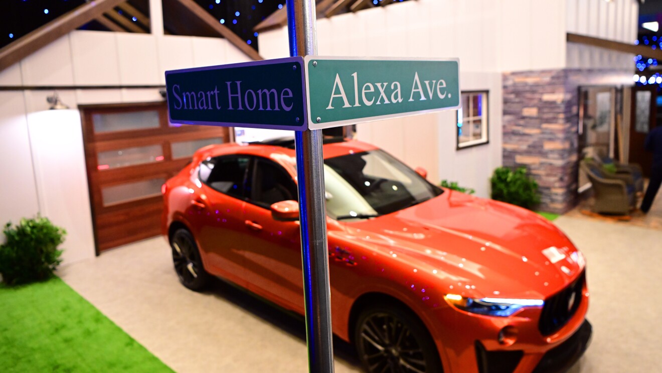 一辆橙色的车停在一条车道上。前景中有一个路牌,其中一条街上写着“智能家居”,另一条街上写着“Alexa大道”。