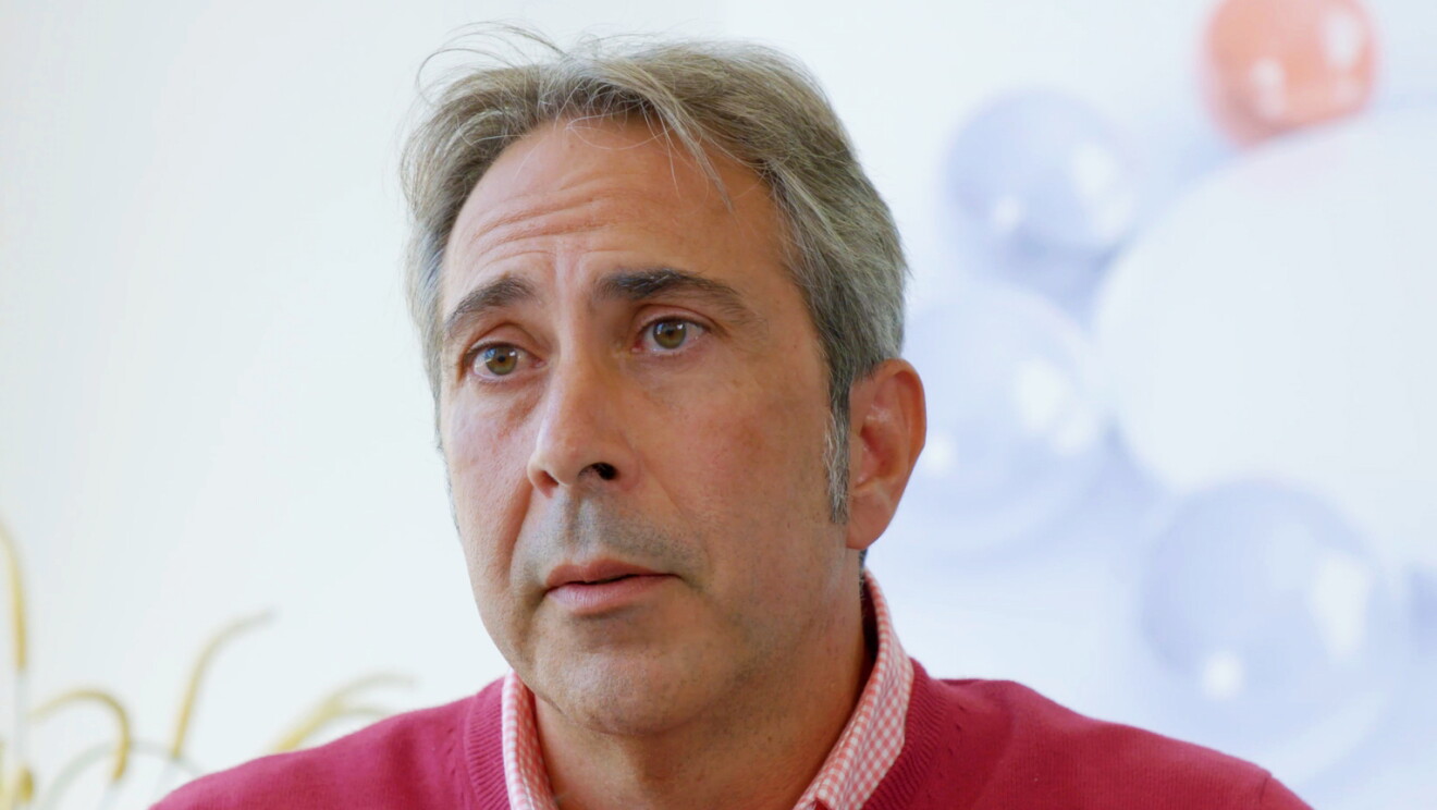 Francisco Ibáñez, socio fundador de Innovatec. Con el pelo blanco y los ojos verdes, lleva una camisa de cuadros blanca y rosa  y un jesey rosa. De fondo una pared blanca y una planta de color verde. 