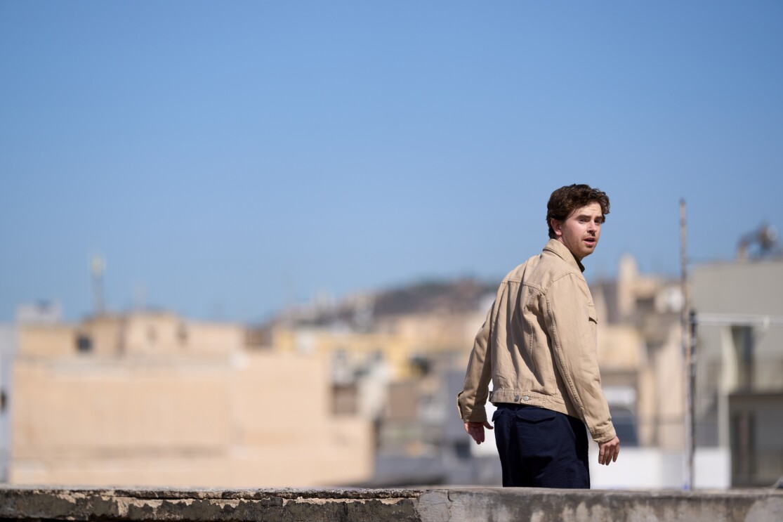 Young man in beige jacket overlooking urban rooftops on sunny day