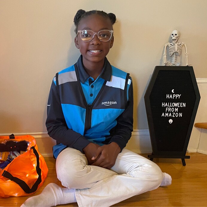 Nyla wears her Amazon delivery driver costume and sits and smiles in her home next to halloween decor.