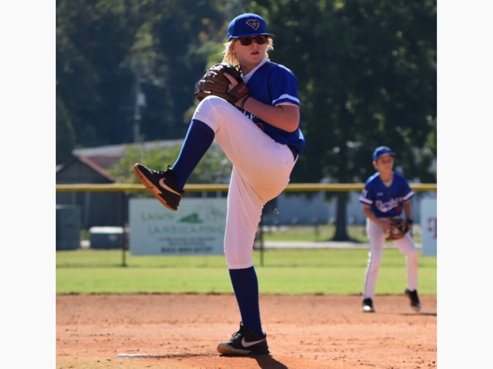 Gavin, preparing to pitch a baseball. He is wearing a baseball uniform and sunglasses.