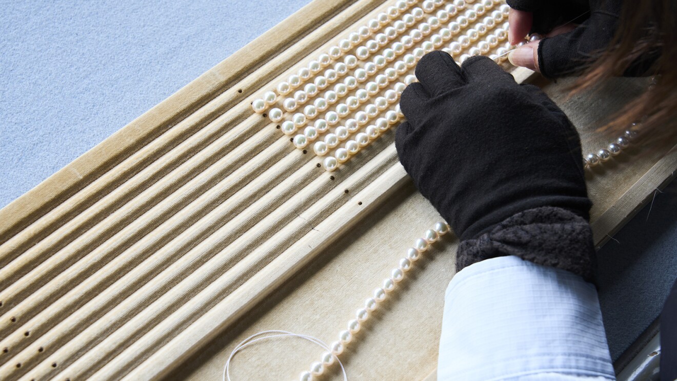 木製のレールの上に置かれ一列に並んだ真珠に手作業で糸を通している様子