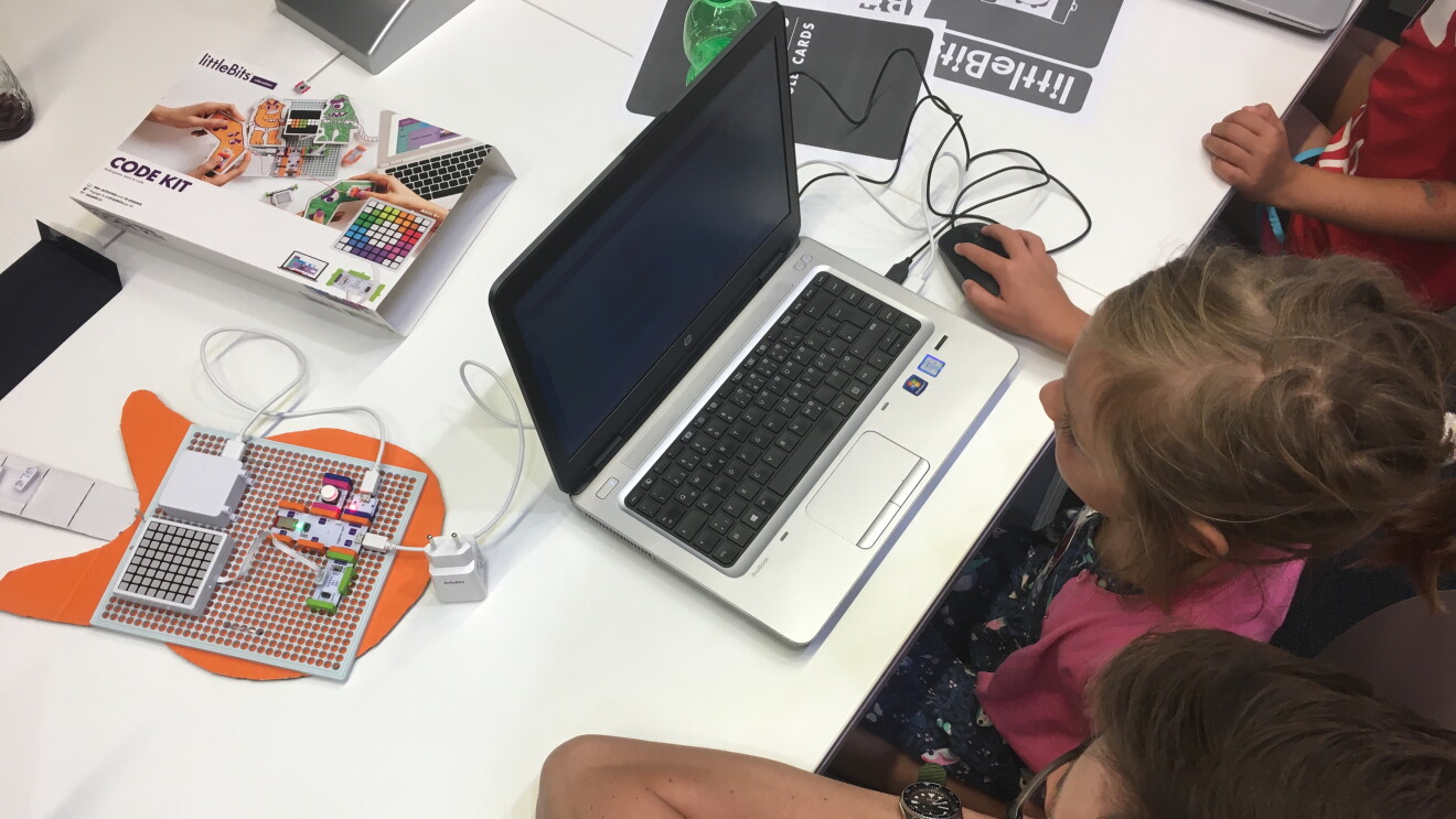 Ein junges Mädchen sitzt am Computer und programmiert. Neben sitzt ein Amazon Mitarbeiter, der ihr hilft und das Programmieren erklärt.