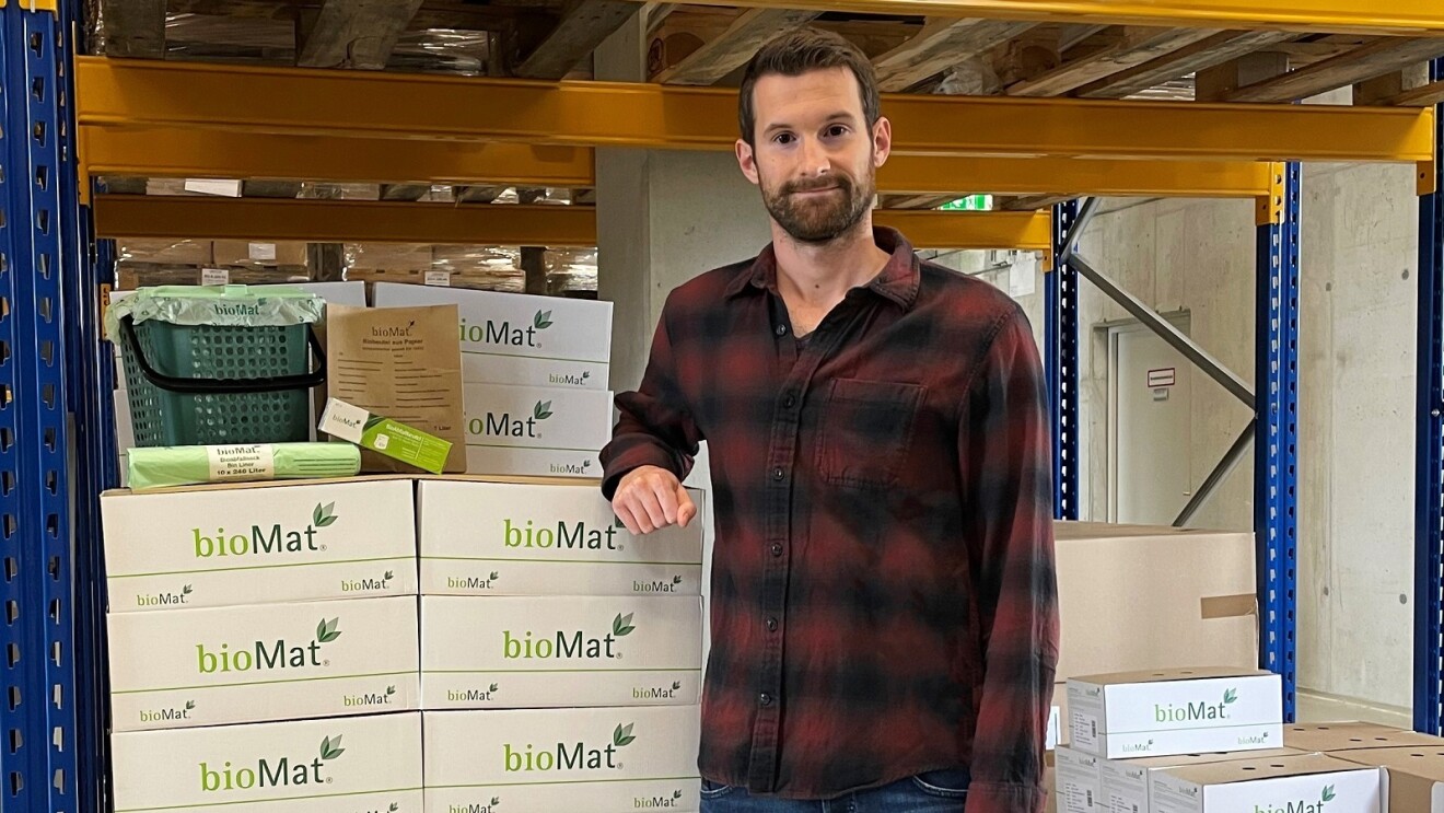 EIn Mann mit einem karierten Hemd steht in einer Lagerhalle neben einem Stapel bioMat-Kartons.