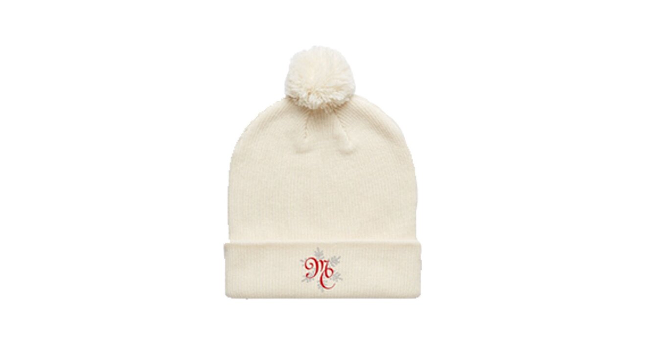 An image of a white beenie hat with a ball on top. There is red embroidered lettering on the front that says "MC"