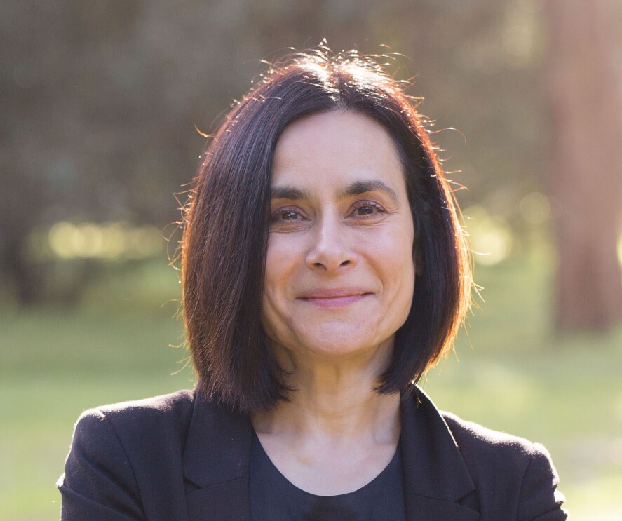 An image of Rose smiling for a photo outside in an area with green grass and trees in the background. 