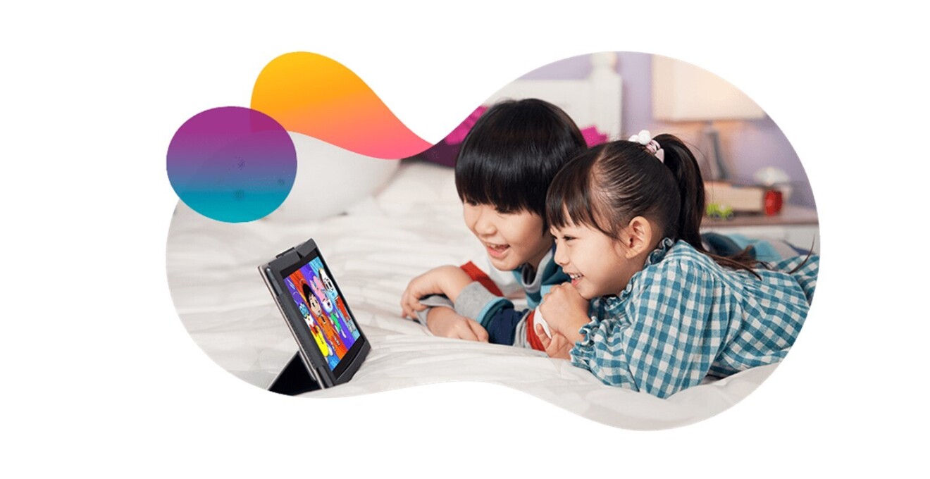 小学生くらいの年齢の男の子と女の子が寝そべりながらタブレットを見ている