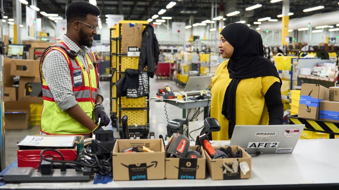 An image of Abdiaziz, an area manager working in an Amazon fulfillment center, speaking to a coworker.