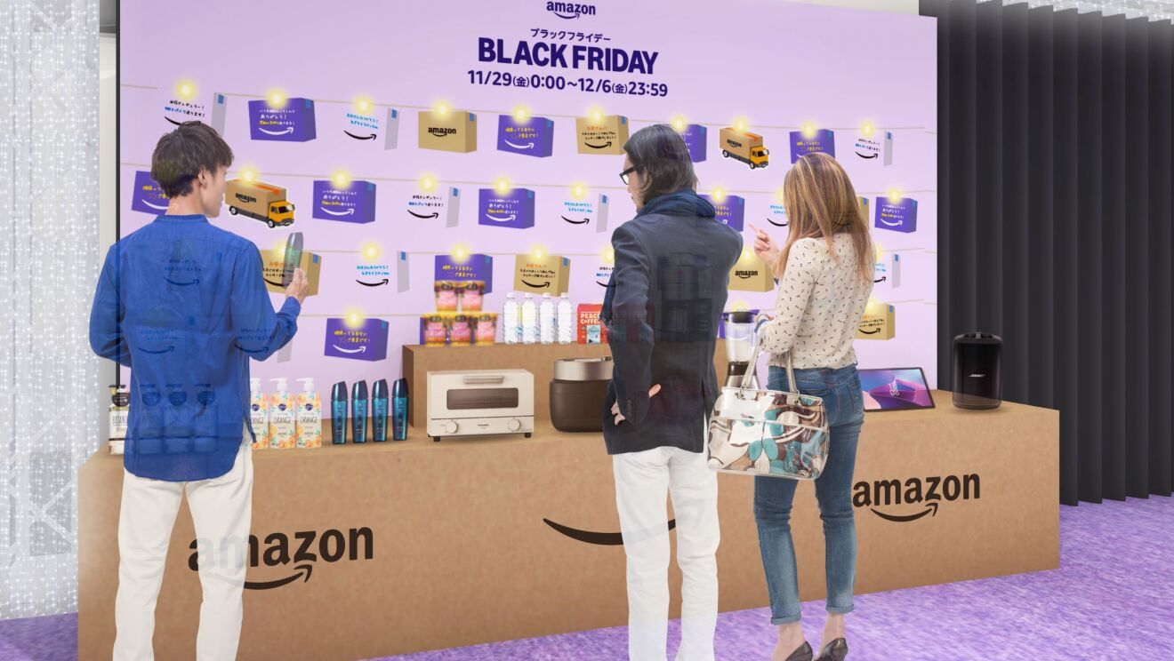 大きなAmazonダンボール箱と似ているテーブルの上には様々な商品が置かれている。そのディスプレイの前で男性2人と女性1人が商品を見ている