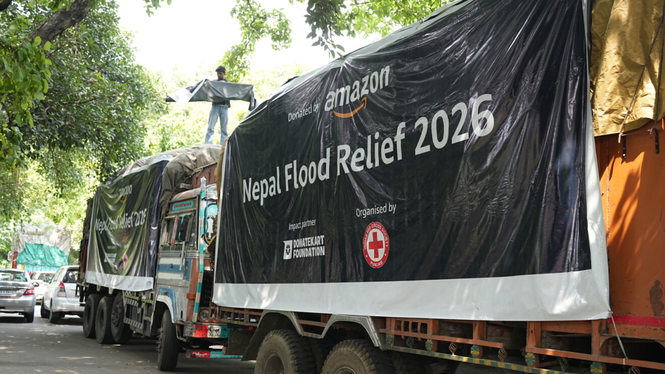 Two trucks with Amazon and charity logos transporting disaster relief items to Nepal