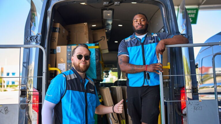 An image of two Amazon delivery drivers standing at the back of a van.