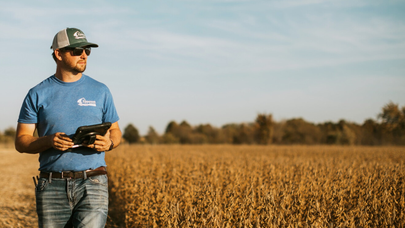 A photo of a farmer out in a field, holding a tablet.