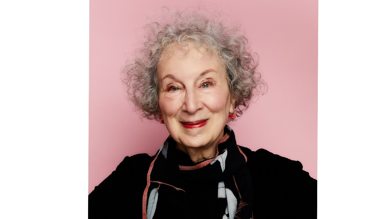 A headshot image of Margaret Atwood smiling in front of a light pink background.