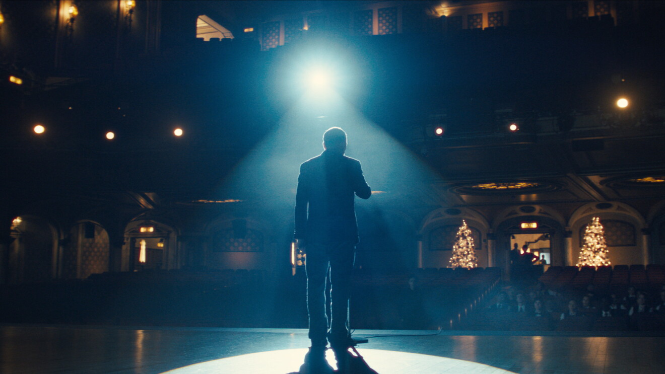 A still from Amazon's 2024 Christmas ad that shows a caretaker stood in front of a microphone, about to sing