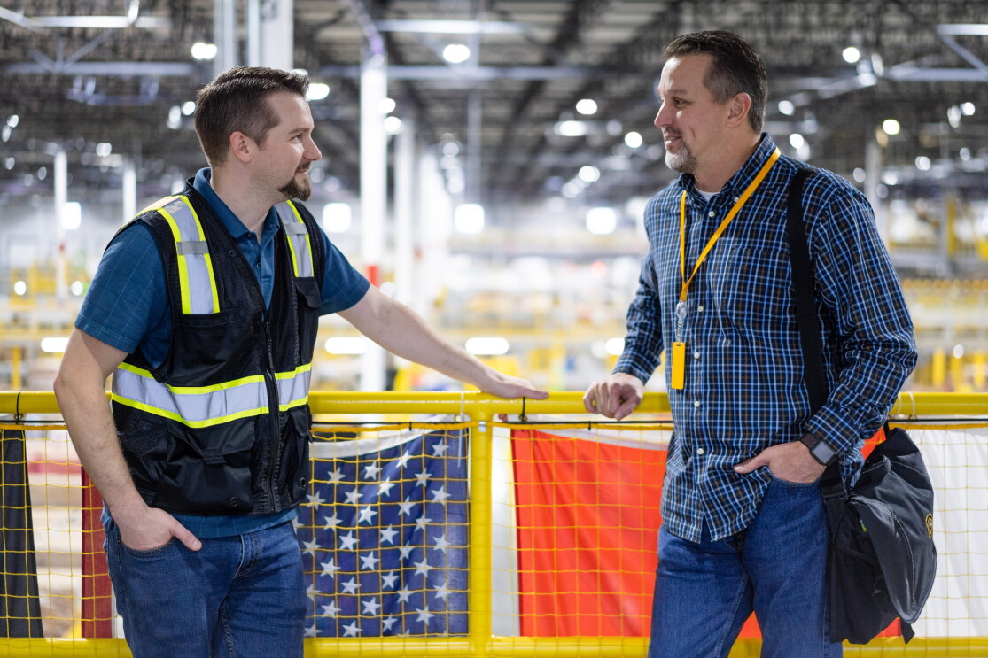 Two men face each other while standing in front of a yellow railing.