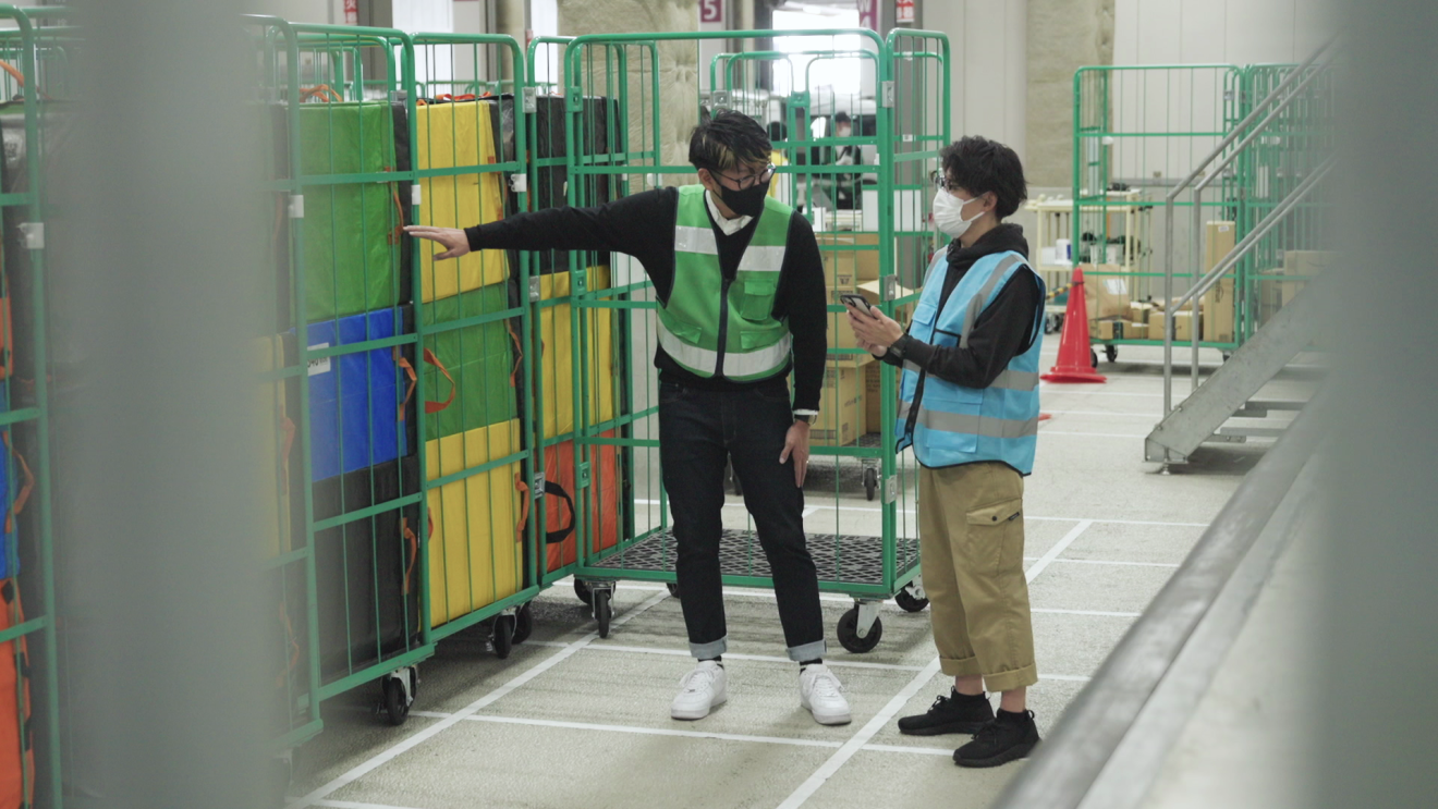 荷物を入れるカートの前で話をする中島さんとドライバー仲間