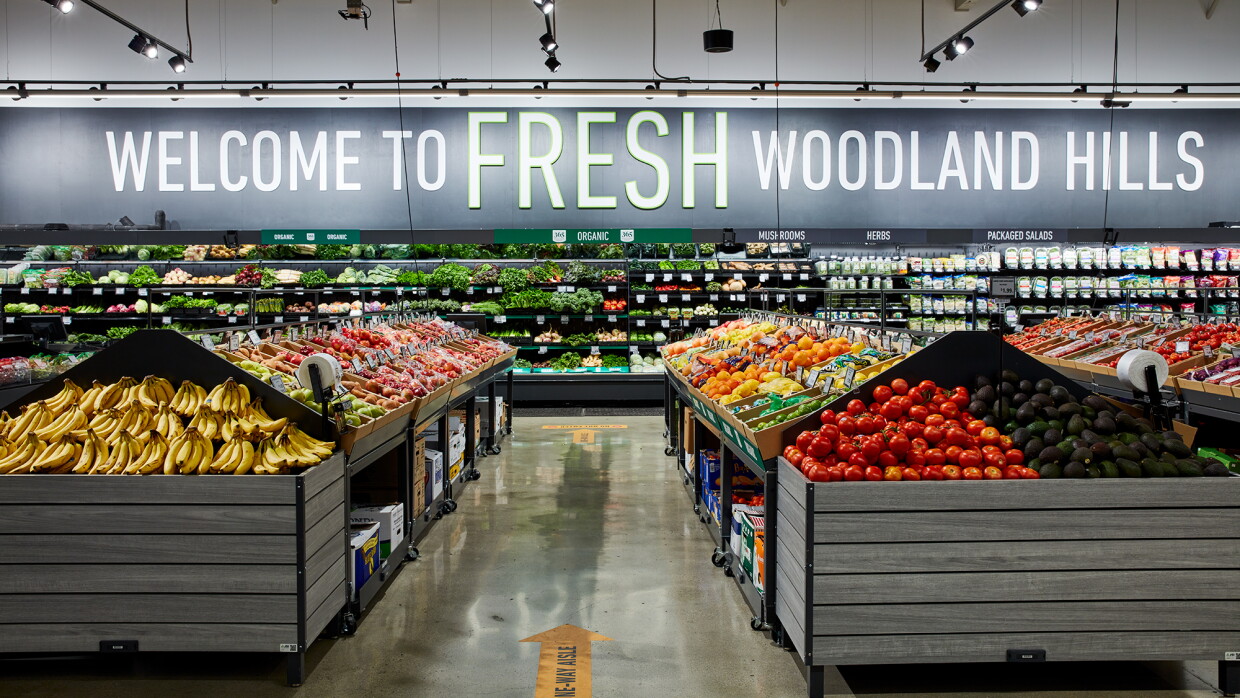 Produce section of a grocery store with the words "WELCOME TO FRESH WOODLAND HILLS" on the back wall.