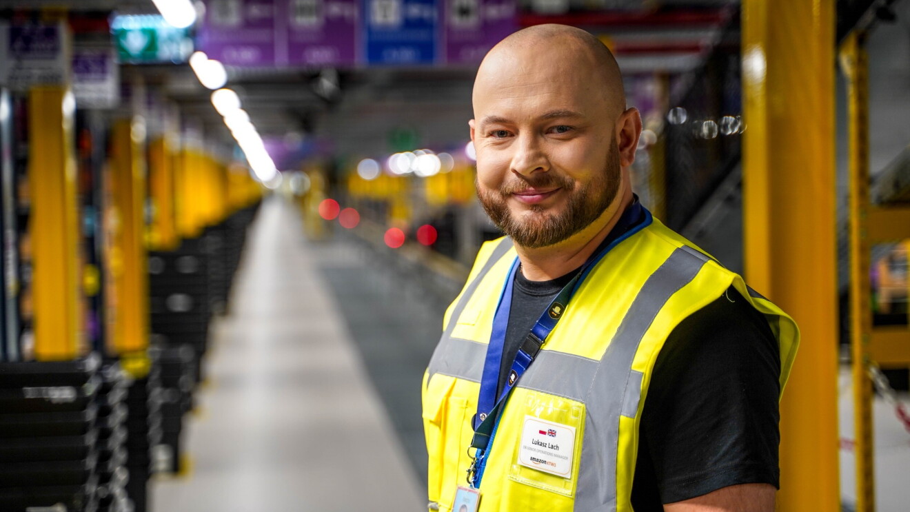 Pracownik Amazon stoi w centrum logistyki i uśmiecha się.