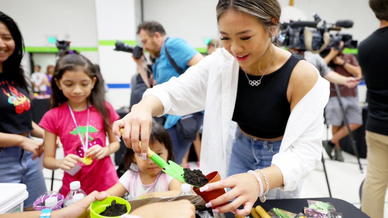 Suni Lee在一个小柱子上播种,学生们站在她旁边。