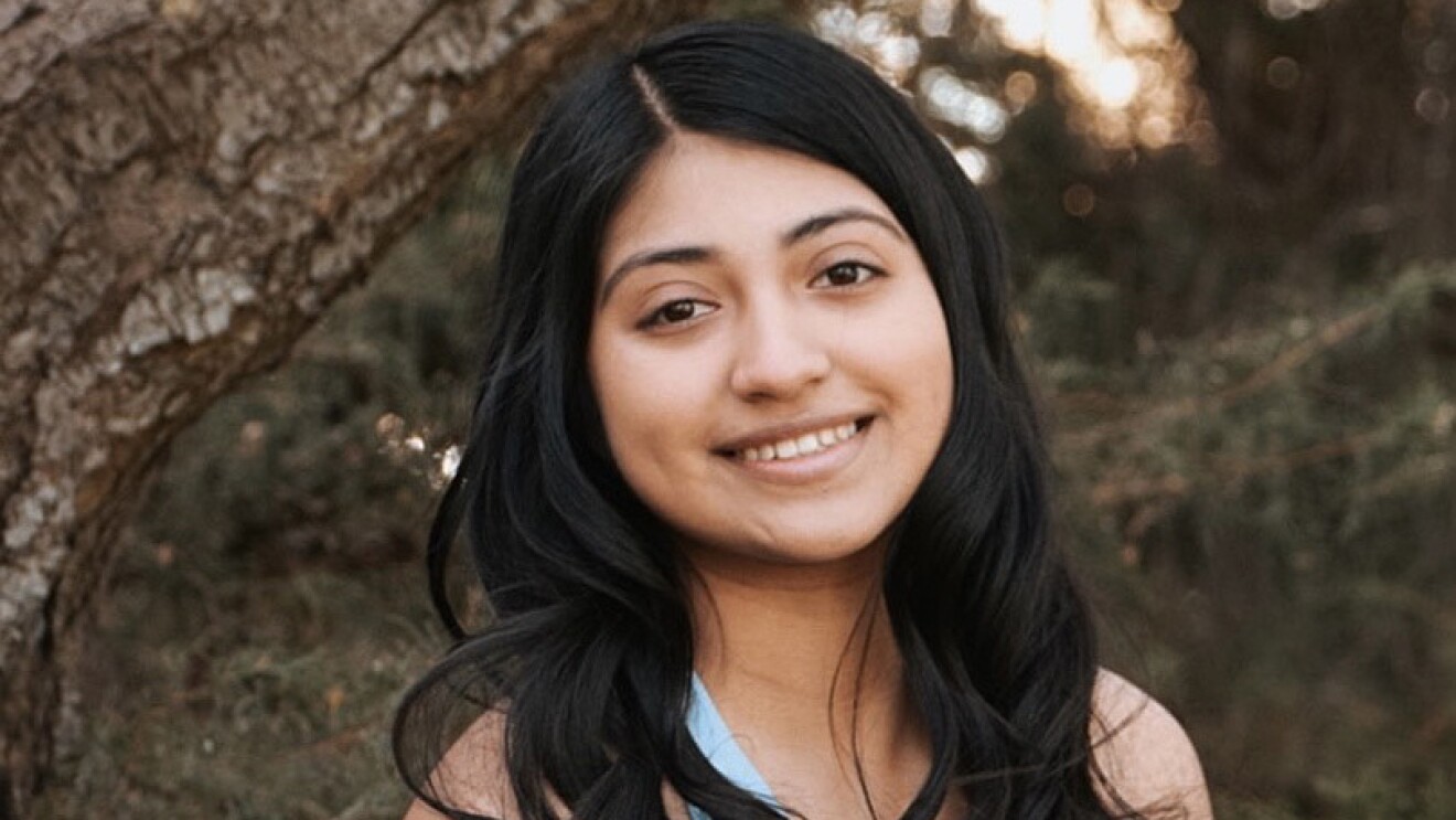 An image of a young woman smiling for a headshot photo in a wooded area.