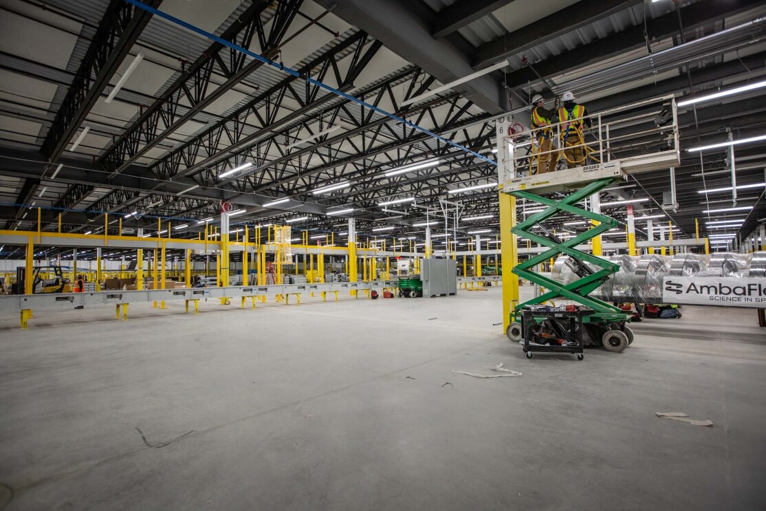 A crew works at building an Amazon Fulfillment center or warehouse in Cleveland, Ohio. Two men stand on a raised platform as they work on the ceiling