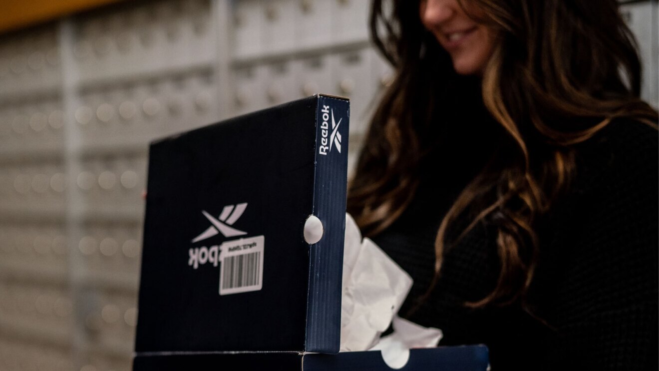 An image of a person opening a Reebok shoe box in a mailroom. There are labels on the box indicating it shipped in the shoe box without additional packaging.