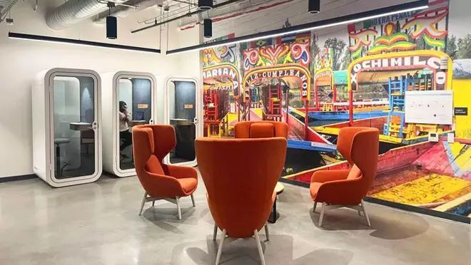 鮮やかな色の遊園地を描いた壁紙が貼られた部屋には、4脚の赤い椅子と3つの白い電話ブースが設置されている。