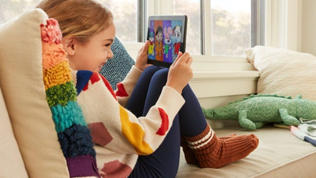 一个小女孩坐在沙发上,微笑着用平板电脑看儿童节目。