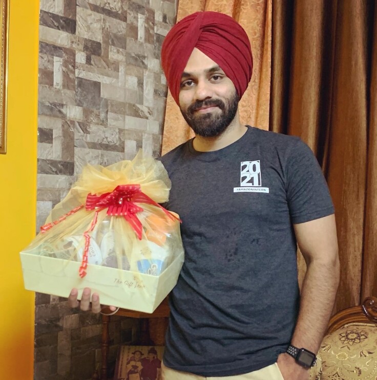 An mage of a man holding a gift basket while smiling for a photo. He is wearing the Amazon 2021 internship class t-shirt.