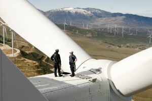 Technicians inspecting wind turbine blades overlooking landscape