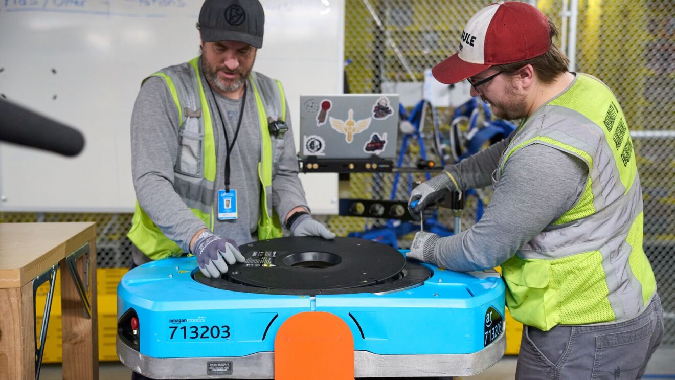 Two Amazon employees work on a robot.