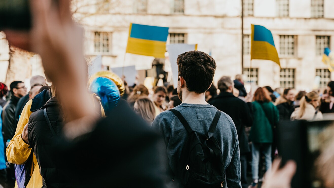 An image of a crowd of people. There are Ukraine flags throughout the crowd and yellow and gold colors showing up on clothing and other items throughout.