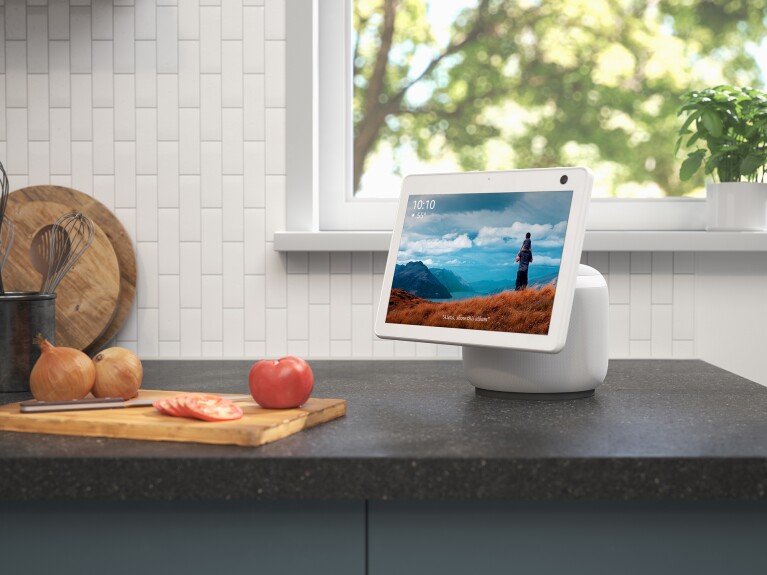 An image of an Echo Show device sitting on a kitchen counter top. A cutting board with food on it sits next to the device.