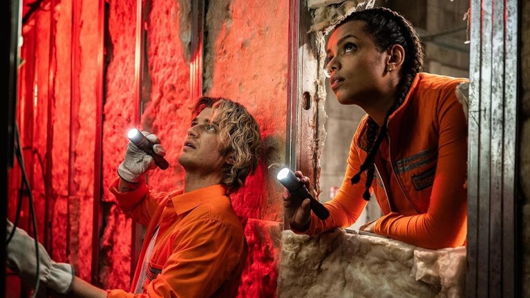 Man and woman wearing maintenance gear use torches to inspect a wall 